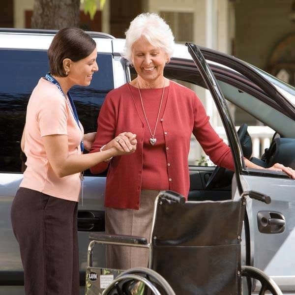 A carer helping an older woman into a car